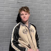 A young man smiling leaning against a gray wall. 