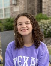 A young lady in a purple sweat shirt smiling. 