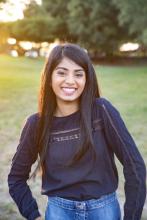 An image of a young lady in a black shirt smiling in the park. 