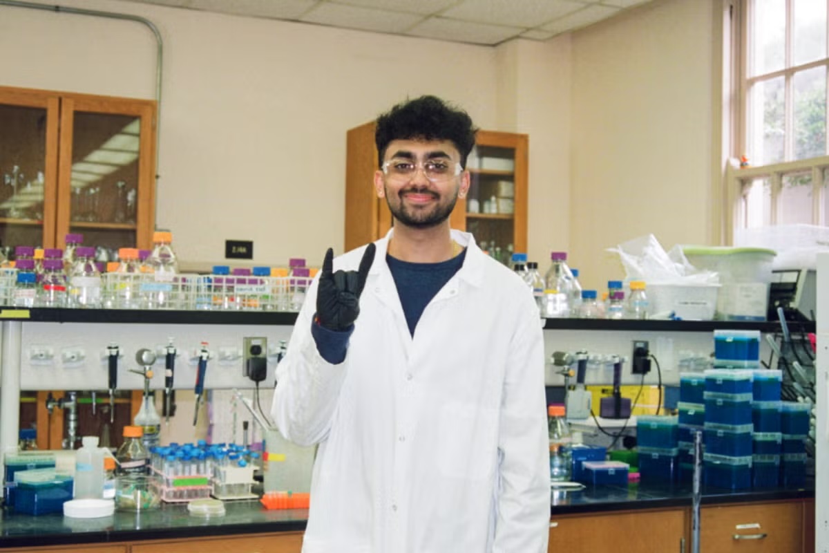 A young man in PPE in a wet lab flashes the hook 'em horns hand sign.
